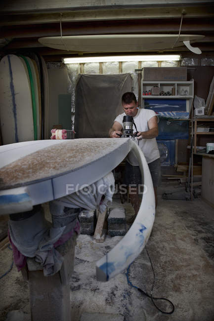 Зрелый человек пилит доску для серфинга в мастерской — стоковое фото
