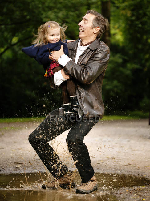 Father holding daughter while splashing in puddle — Stock Photo