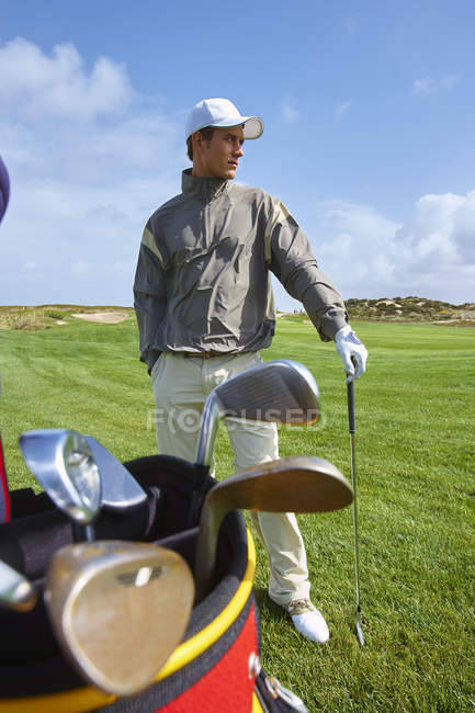 Golfista sosteniendo el club de oro, mano en bolsillo, mirando hacia otro lado - foto de stock