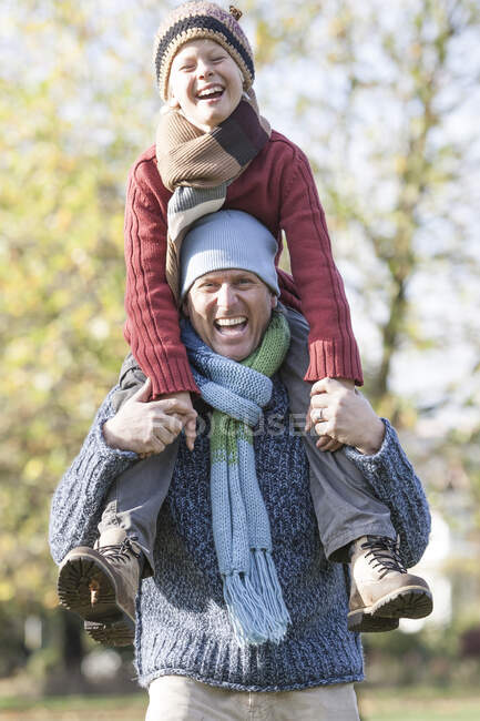 Padre e hijo en el parque, padre llevando a su hijo en hombros, riendo - foto de stock