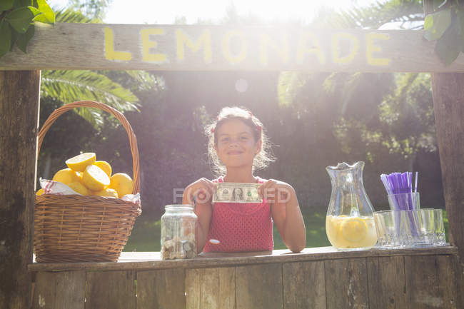 Portrait of proud girl on lemonade stand holding up one dollar bill — Stock Photo