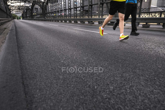 Piernas de dos hombres corriendo por el puente de la ciudad - foto de stock