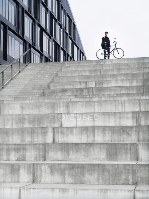 Urban cyclist with bicycle standing on top of stairway — Stock Photo