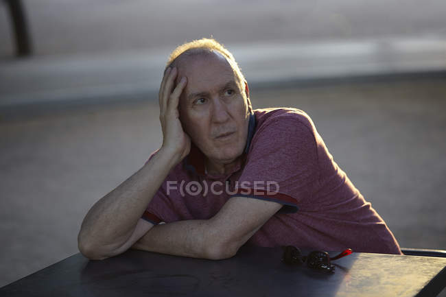 Hombre mayor sentado en la mesa, descansando sobre el codo - foto de stock