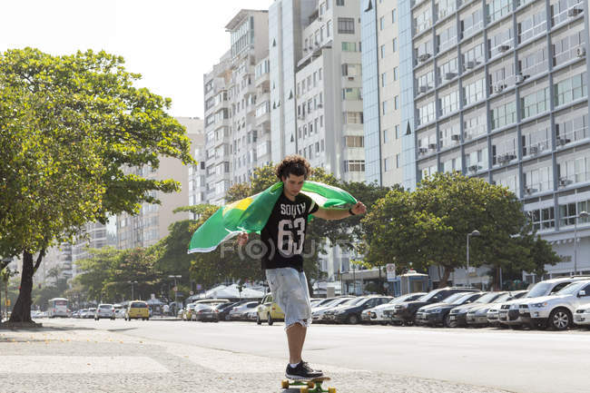 Jeune homme skateboard tenant le drapeau brésilien, Copacabana, Rio De Janeiro, Brésil — Photo de stock