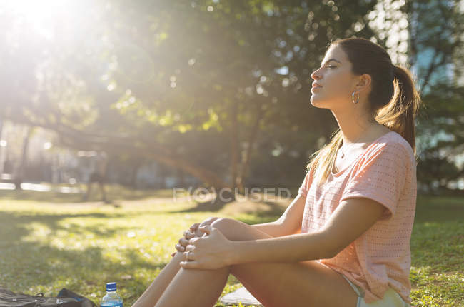 Mujer joven sentada en el parque con los ojos cerrados, Manila, Filipinas - foto de stock