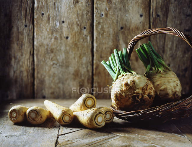 Parsnips and celeriac in wicker basket on wood — Stock Photo