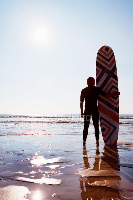 Uomo in piedi sulla spiaggia con tavola da surf — Foto stock