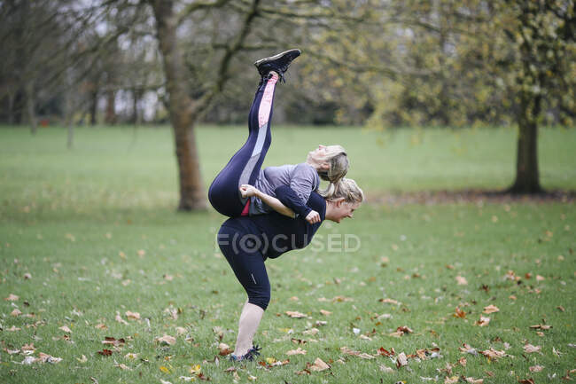 Две женщины делают упражнения спина к спине в парке — стоковое фото