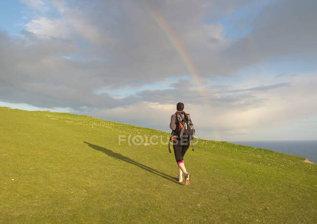 Junge Frau wandert auf Hügel in Richtung Regenbogen, Rückansicht — Stockfoto