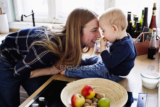 Femme jouant avec bébé fils sur le comptoir de la cuisine — Photo de stock