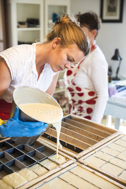 Young woman pouring liquid lavender soap into moulds in handmade soap workshop — Stock Photo
