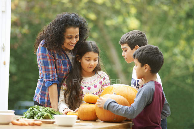 Mère mature et trois enfants admirant les citrouilles maison dans la cuisine — Photo de stock
