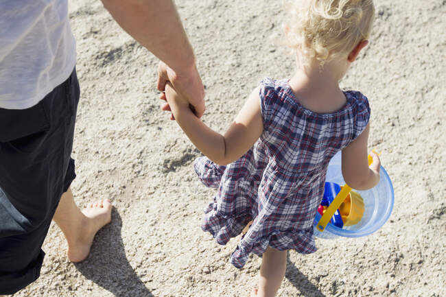Padre y niña paseando por la playa con un cubo de juguete - foto de stock