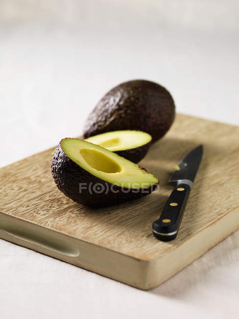 Avocado con coltello su tavola di legno — Foto stock