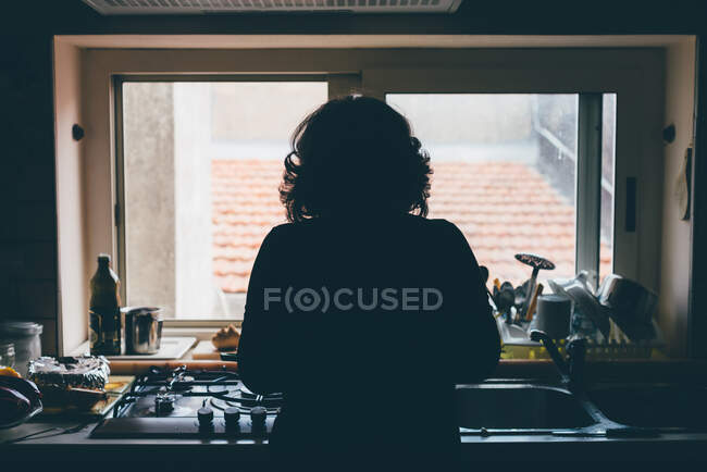 Visão silhueta traseira da mulher em pé na frente da pia da cozinha — Fotografia de Stock