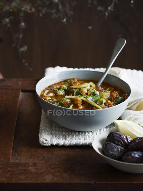 Harira soup in bowl with dates and lemon wedge — Stock Photo