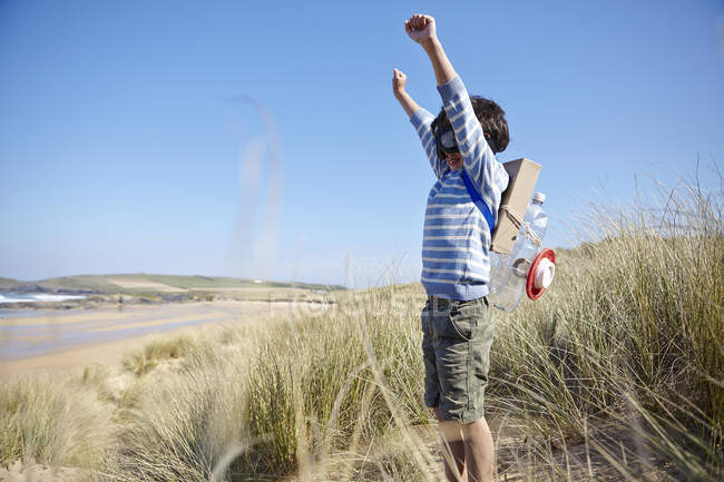 Young boy on beach, wearing fancy dress, arms raised — Stock Photo