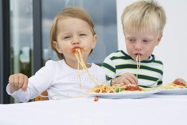 Boy and female toddler eating spaghetti on patio — Stock Photo