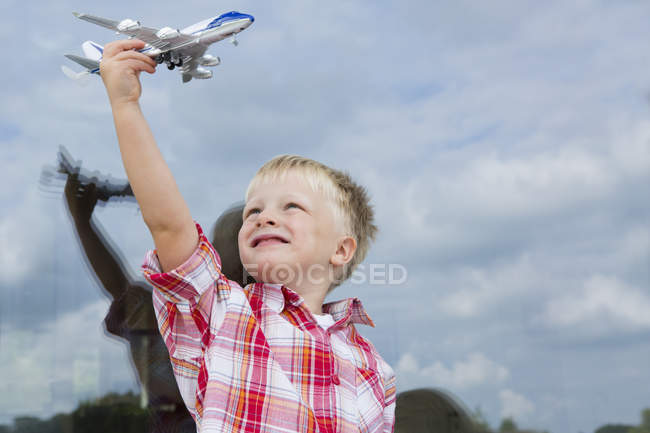 Boy holding up toy airplane in front of house window — Stock Photo