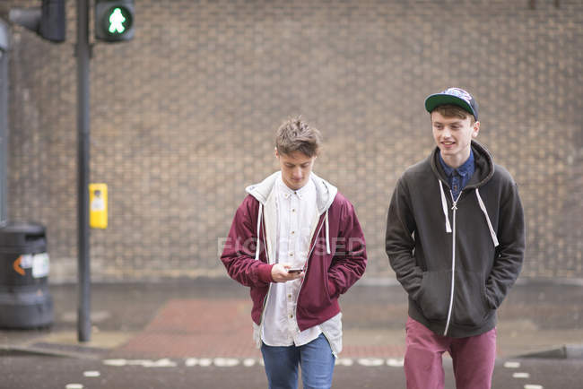 Dos amigos varones cruzando la calle en la ciudad - foto de stock