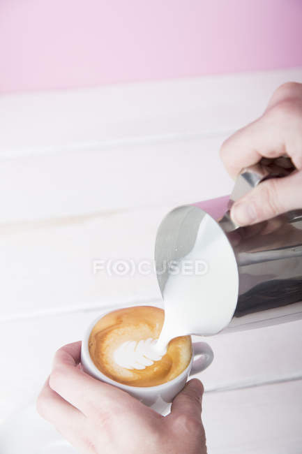 Manos Mans verter leche espumosa en la taza de café - foto de stock