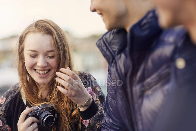 Tres amigos al aire libre, mujer joven sosteniendo la cámara, riendo, Bristol, Reino Unido - foto de stock