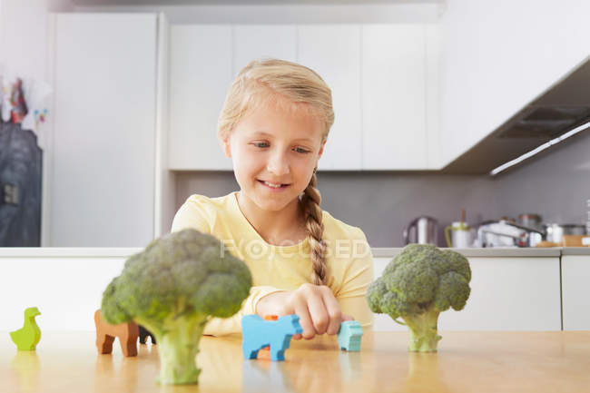 Chica jugando con animales de juguete alrededor de brócoli - foto de stock