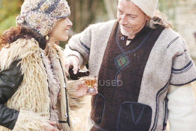 Maduro hippy pareja verter vaso de sidra en el jardín - foto de stock