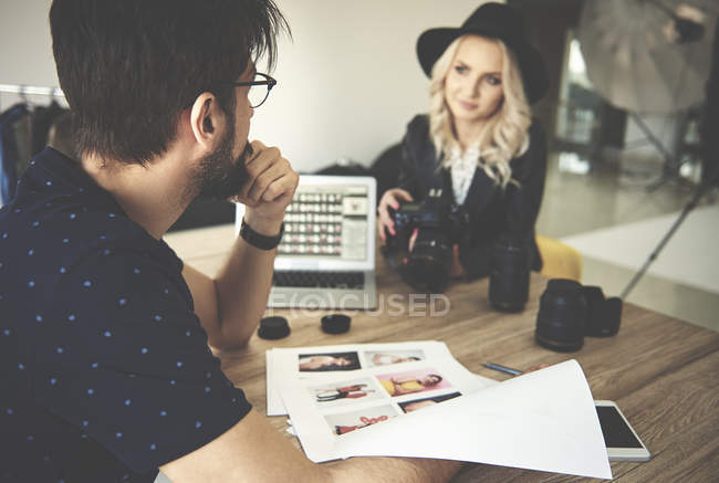 Photographer and stylist woman sitting at table and looking at photographs in photography studio — Stock Photo