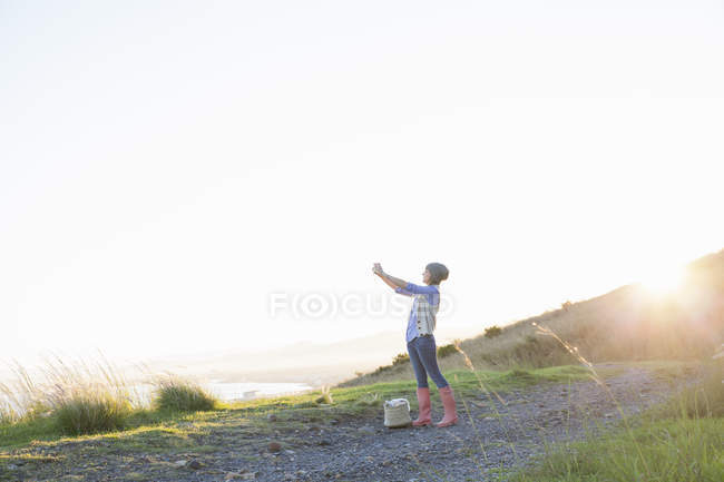 Jeune femme prenant des photos sur la colline au coucher du soleil — Photo de stock