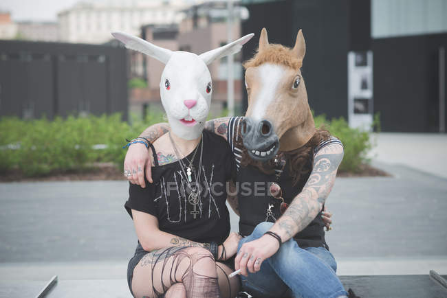 Retrato de pareja hippy punk con conejo y máscaras de disfraces de caballo - foto de stock