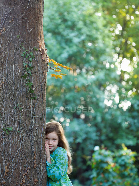 Chica joven apoyada en el árbol en el jardín - foto de stock