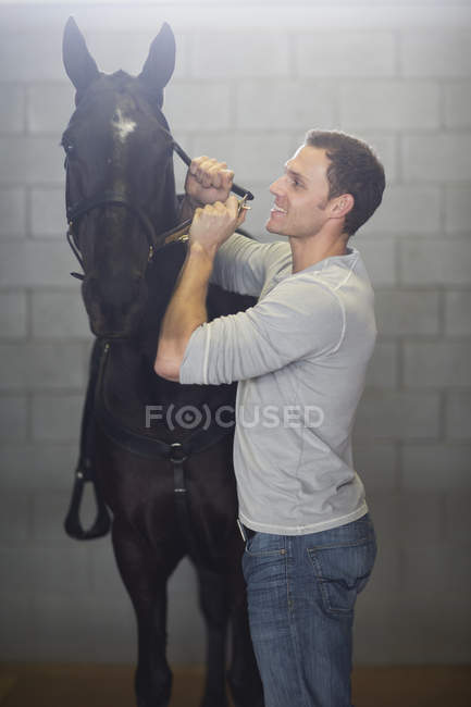Masculino stablehand colocando freio no cavalo no estábulos — Fotografia de Stock
