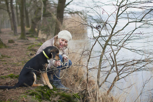 Mujer adulta agachada con su perro en la orilla del río - foto de stock