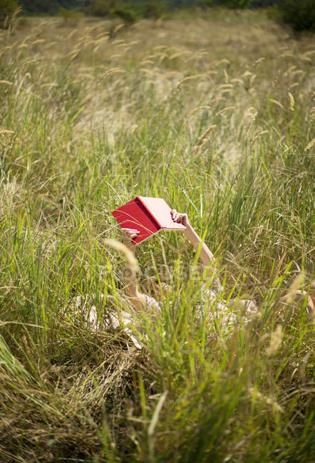 Mulher deitada em livro de leitura de grama longa — Fotografia de Stock