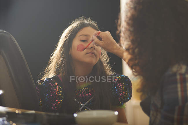 Mother painting daughter rosy cheeks for Halloween — Stock Photo