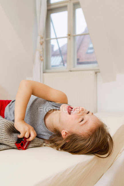 Lächelndes Mädchen spielt mit Spielzeugbus im Bett — Stockfoto