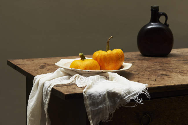 Pumpkins in serving dish on table with brown glass bottle — Stock Photo