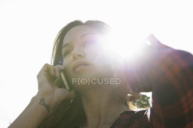 Junge Frau spricht mit Smartphone gegen sonnigen Himmel — Stockfoto