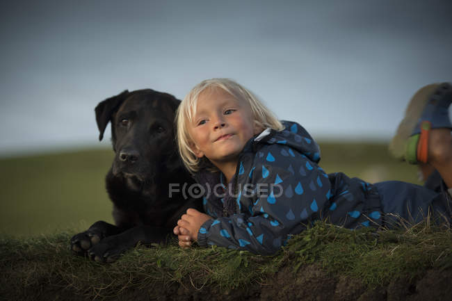 Молодий хлопчик лежить з собакою в полі — стокове фото