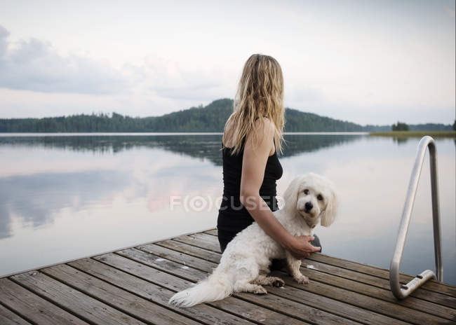 Mulher com cotão de tulear cão olhando para fora do cais do lago, Orivesi, Finlândia — Fotografia de Stock