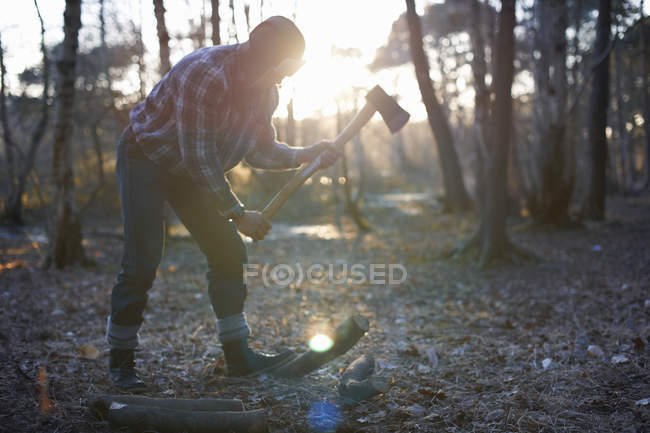 Mature male backpacker chopping logs for campfire in forest — Stock Photo