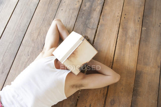 Uomo sdraiato su assi di legno con libro sul viso — Foto stock