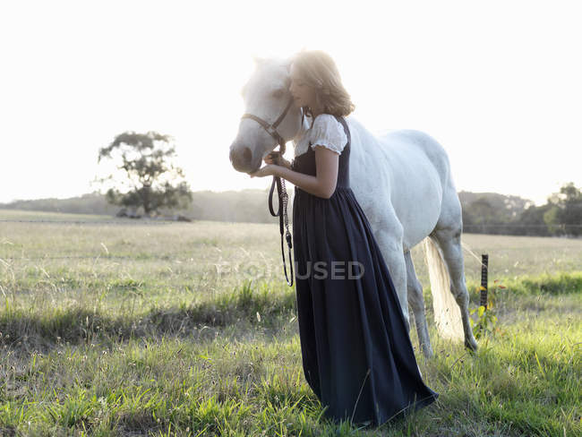 Retrato de menina adolescente com cavalo cinza no campo iluminado pelo sol — Fotografia de Stock