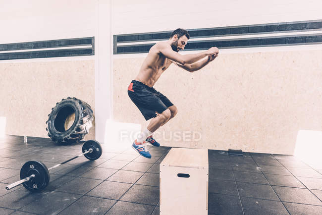 Young man jumping on box in cross training gym — Stock Photo