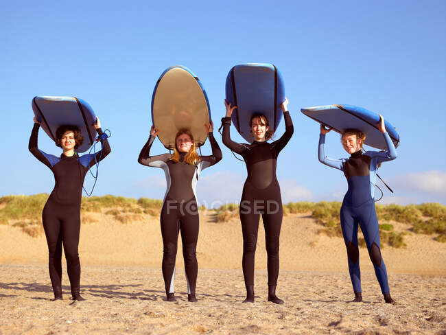 Cuatro surfistas femeninas de pie en una playa - foto de stock