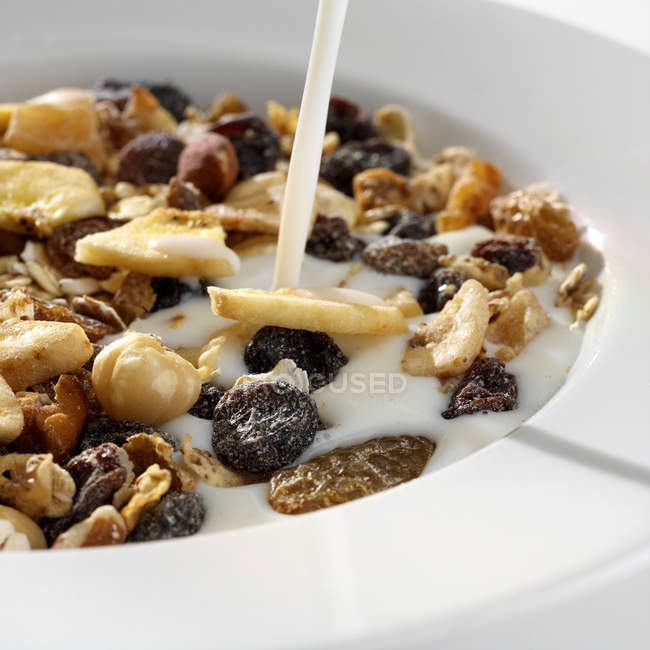 Milk pouring in bowl of muesli, close up shot — Stock Photo