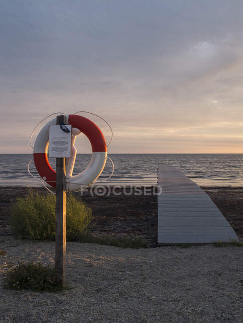 Holzpromenade und Rettungsring am Strand bei Sonnenuntergang — Stockfoto