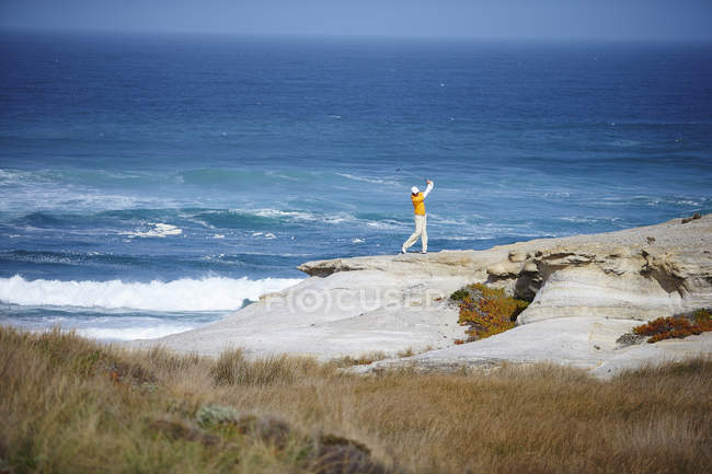 High angle view of golfer standing on cliff overlooking ocean taking golf swing — Stock Photo